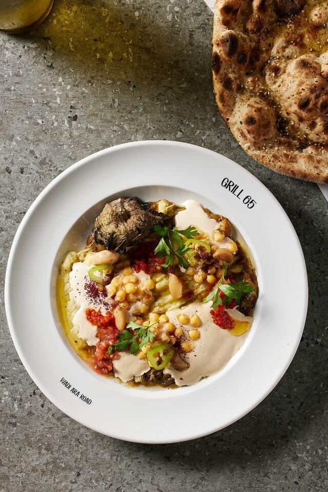 חציל שלם קלוי ומפוצח לאורכו, מונח על טחינה לבנה ומפוזר בגרגירי חומוס ושקדים