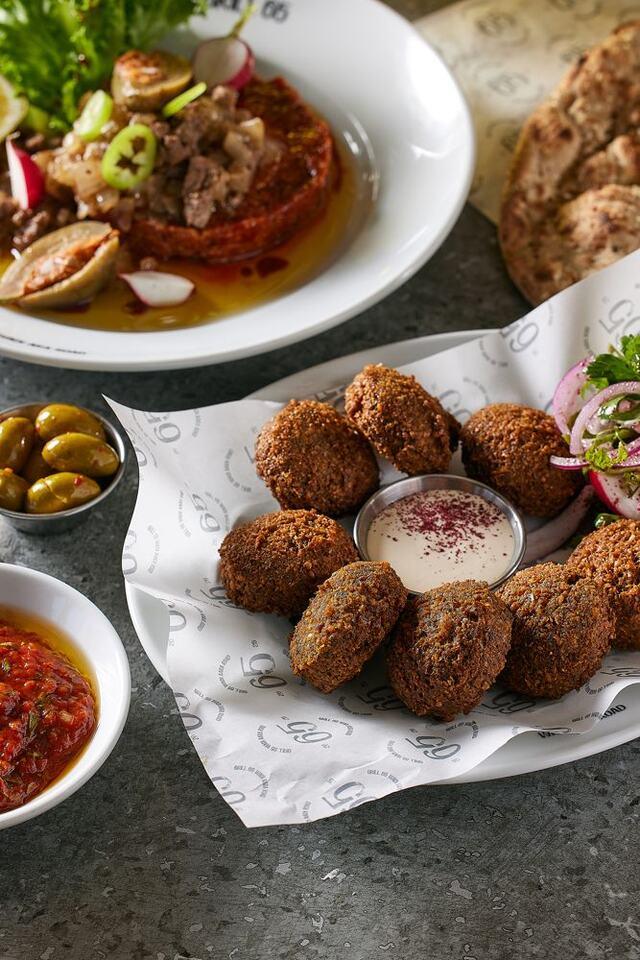 כדורי פלאפל זהובים ופריכים ערוכים בצלחת לצד קערית טחינה לבנה