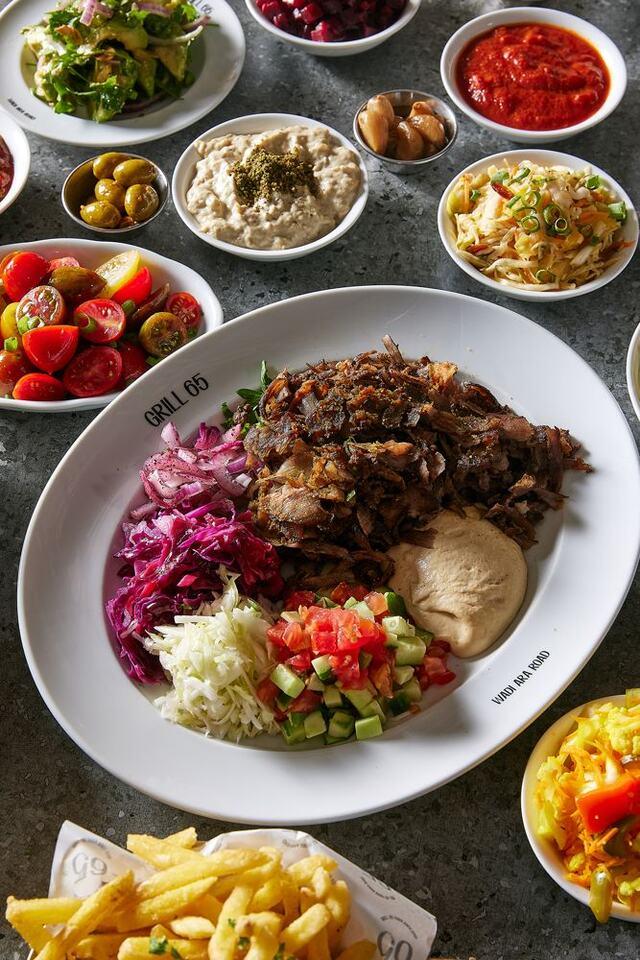 ערימת שווארמה עגל פרוסה דק בצלחת, עם טפטוף טחינה לבנה ופטרוזיליה